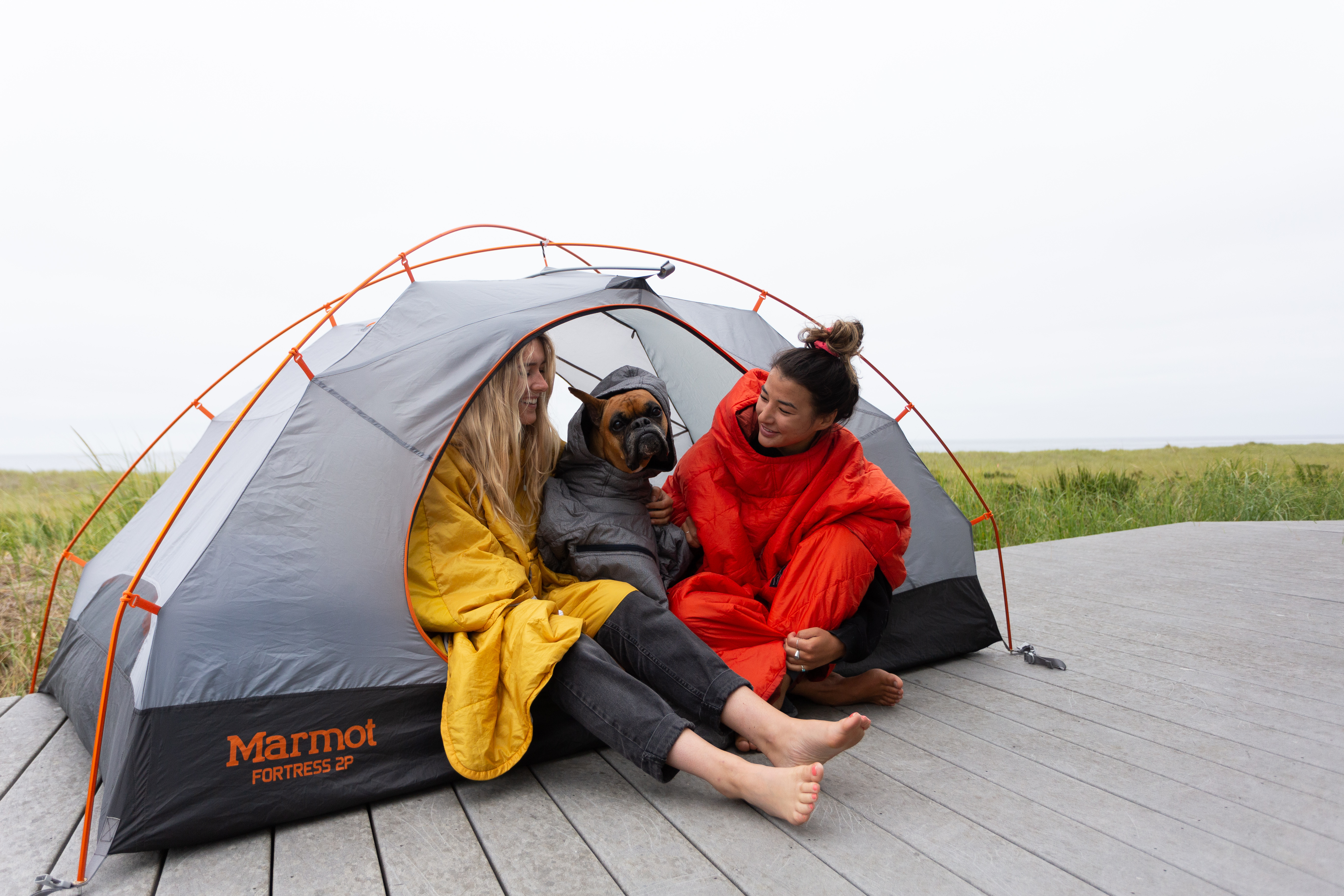 2 girls in a tent wearing ponchos with a dog
